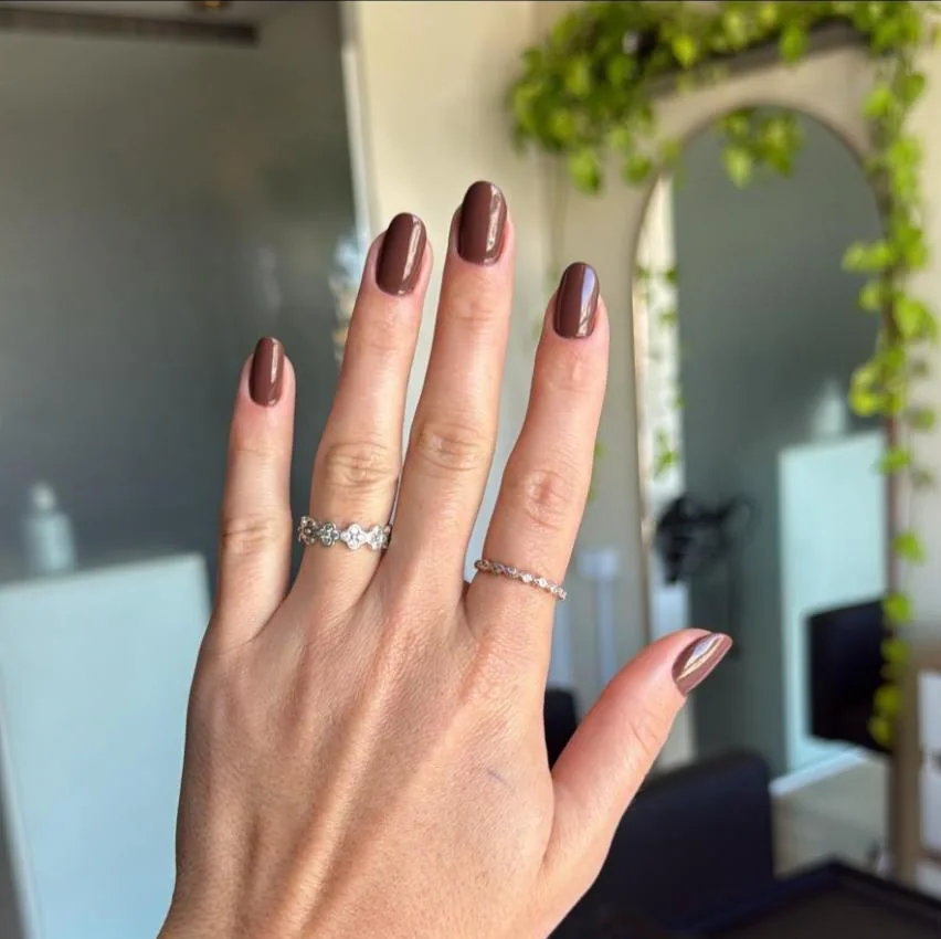 Mão com unhas curtas esmaltadas em marrom, no salão
